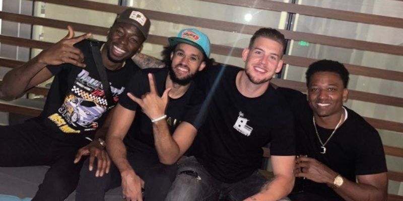 Left to right: Amida Brimah, Derrick White, Alex Welsh, Tommie Anderson. All four adults are wearing casual outfits. White is wearing a San Antonio Spurs hat.